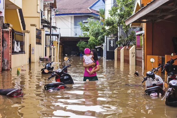 Женщина несет на руках ребенка по затопленной улице индонезийского города Макасар - Sputnik Азербайджан