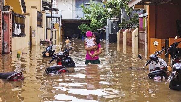 Женщина несет на руках ребенка по затопленной улице индонезийского города Макасар - Sputnik Azərbaycan