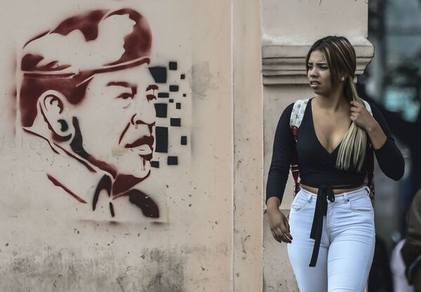 Женщина проходит мимо изображения бывшего президента Венесуэлы Уго Чавеса в Каракасе - Sputnik Азербайджан