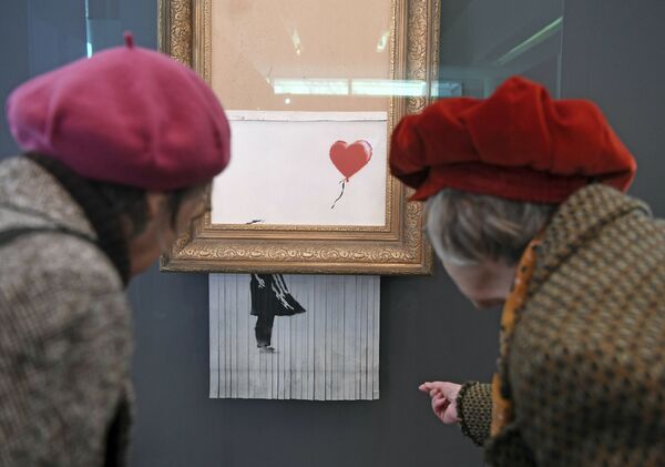 Посетители смотрят на самоуничтожившуюся после продажи на аукционе картину художника Бэнкси Девочка с воздушным шаром, которая теперь называется Любовь в мусорном баке, в Музее современного искусства в Баден-Бадене, Германия - Sputnik Азербайджан
