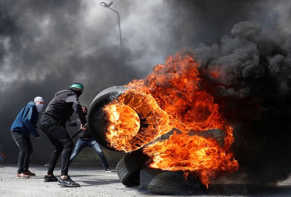 Палестинский демонстрант с горящей шиной во время столкновений с израильскими войсками возле еврейского поселения Бейт-Эль на оккупированном Израилем Западном берегу - Sputnik Азербайджан