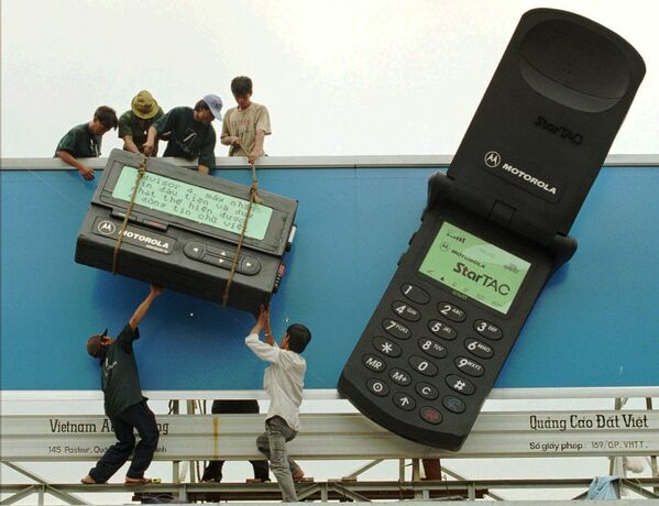 Рабочие размещают гигантский пейджер рядом с гигантским мобильным телефоном с рекламой телекоммуникационных продуктов Motorola в городе Хошимин, 1996 - Sputnik Азербайджан