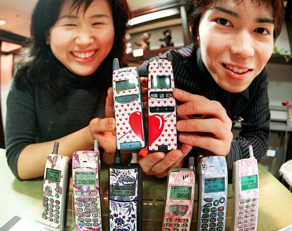 Молодая японская пара демонстрирует свои мобильные телефоны с дизайнерскими клеймами в универмаге Токи - Sputnik Азербайджан