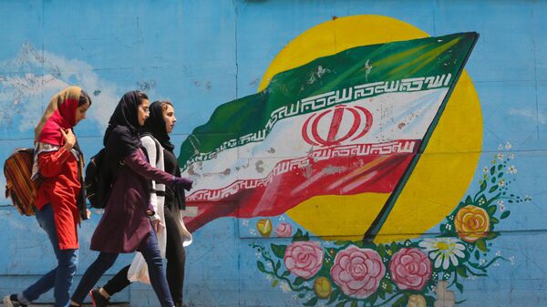  Молодые девушки проходят перед фреской, на которой изображен иранский национальный флаг в центре столицы Тегерана - Sputnik Azərbaycan