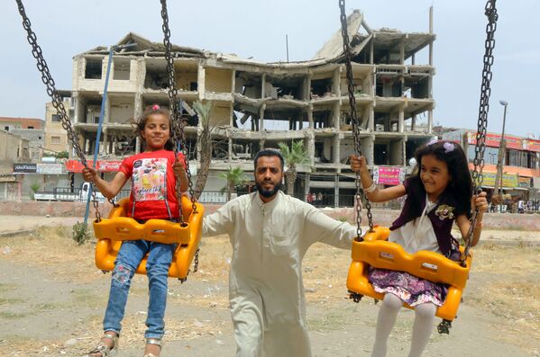 Девочки катаются на качелях возле поврежденного здания в первый день мусульманского праздника Ид аль-Фитр в городе Ракка, Сирия - Sputnik Азербайджан