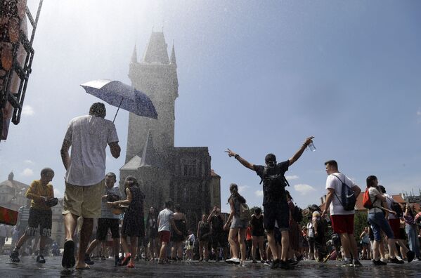 Люди охлаждаются под струей воды в жаркий и летний день на Староместской площади в Праге, Чехия - Sputnik Azərbaycan
