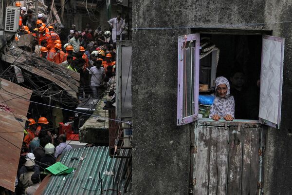 Местная жительница смотрит в окно, пока спасатели ищут выживших после обрушения здания в Мумбаи, Индия - Sputnik Азербайджан