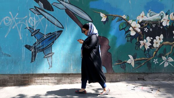 Женщина проходит мимо настенной росписи вдоль стены бывшего посольства США в иранской столице Тегеране - Sputnik Азербайджан