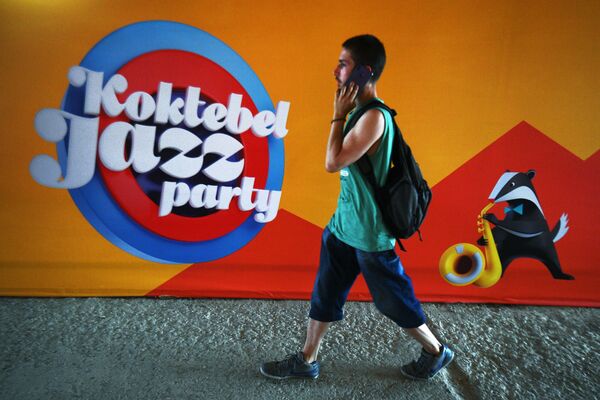 Молодой человек на фоне баннера ежегодного международного джазового фестиваля Koktebel Jazz Party в Коктебеле - Sputnik Азербайджан