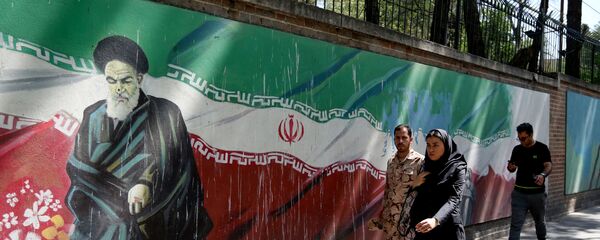 Люди проходят мимо фрески с изображением основателя исламской республики аятоллы Рухоллы Хомейни и государственного флага вдоль стены бывшего посольства США в иранской столице Тегеране 22 июня 2019 года - Sputnik Азербайджан