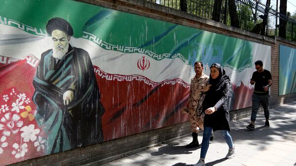 Люди проходят мимо фрески с изображением основателя исламской республики аятоллы Рухоллы Хомейни и государственного флага вдоль стены бывшего посольства США в иранской столице Тегеране 22 июня 2019 года - Sputnik Азербайджан