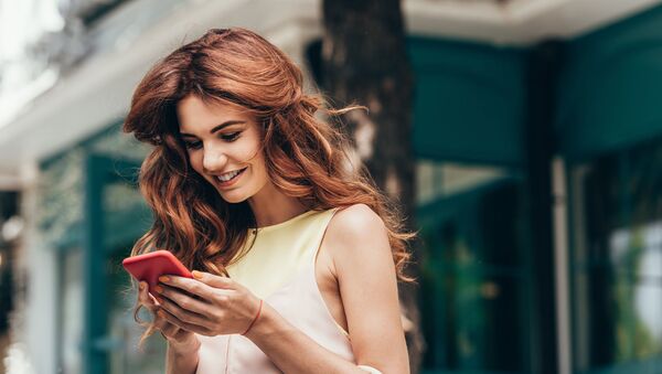 Красивая рыжеволосая девушка улыбается и смотрит в свой смартфон - Sputnik Азербайджан