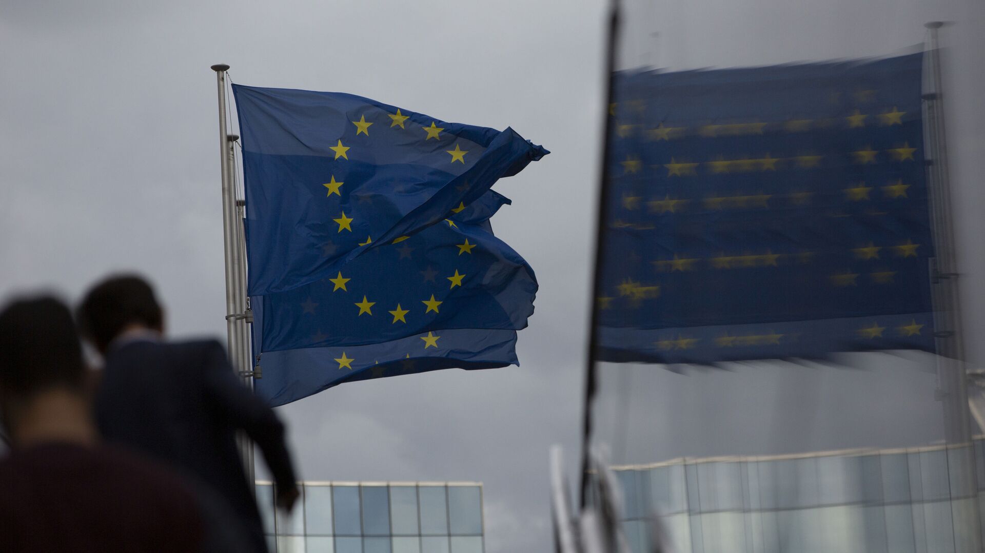 Флаги Европейского Союза развеваются на ветру, когда два человека поднимаются по лестнице возле штаб-квартиры ЕС в Брюсселе - Sputnik Азербайджан, 1920, 24.01.2023