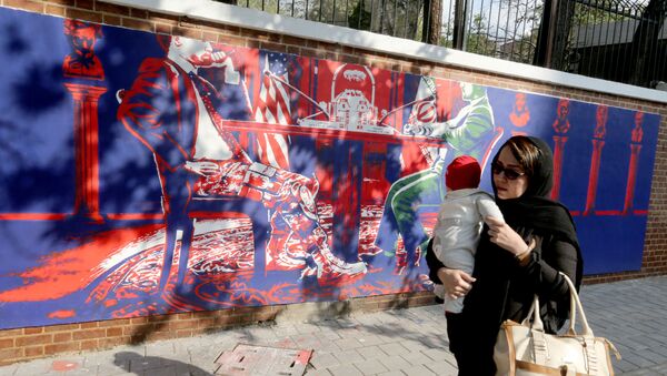 Иранская женщина с ребенком на руках проходит мимо бывшего посольства США в столице в Тегеране - Sputnik Azərbaycan