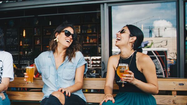 Две девушки в солнечных очках с бокалами пива в руке разговаривают и смеются - Sputnik Азербайджан
