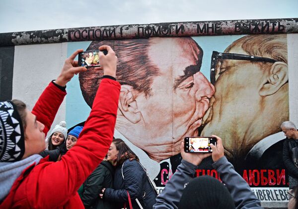 Люди у фрагмента Берлинской стены (East-Side Gallery) на Мюленштрассе с произведением Дмитрия Врубеля Господи! Помоги мне выжить среди этой смертной любви или Братский поцелуй (поцелуй Брежнева и Хонеккера) - Sputnik Азербайджан
