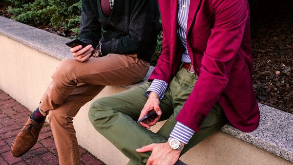 Двое мужчин в стильной молодежной одежде сидят и держат смартфоны - Sputnik Азербайджан