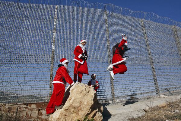 Палестинцы в рождественских костюмах прыгают со скалы у израильского разделительного барьера - Sputnik Азербайджан