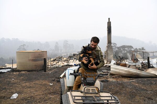 Мужчина с собакой на фоне сгоревшего дома в Австралии - Sputnik Азербайджан