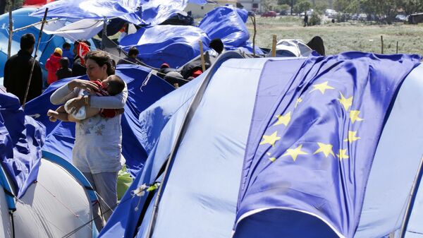 Беженка с ребенком на фоне флага ЕС в палаточном лагере для мигрантов и беженцев в Греции - Sputnik Азербайджан