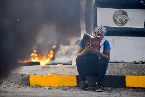 Участник антипровительственных протестов читает роман на фоне горящих шин, Эн-Наджаф, Ирак - Sputnik Azərbaycan
