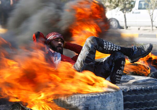 Демонстрант среди горящих шин, блокирующих дорогу во время антиправительственных акций протеста в Наджафе, Ирак - Sputnik Азербайджан