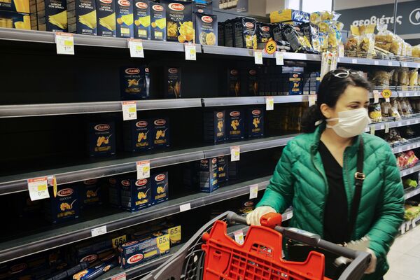 A woman wearing a protective face mask passes by a partly empty self of pasta as she shops in a super market in Athens, Greece - Sputnik Азербайджан