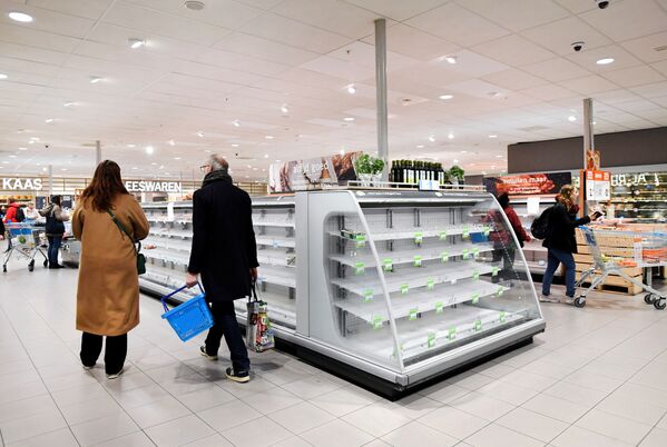 Shoppers walk by near-empty shelves at a supermarket in Amsterdam as people hoard food because of the coronavirus outbreak, - Sputnik Азербайджан