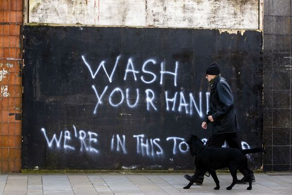Мужчина с собакой напротив граффити с призывом мыть руки в Северной Ирландии  - Sputnik Азербайджан
