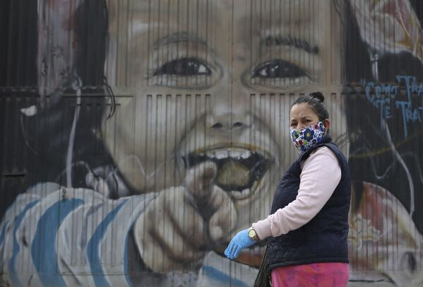 Женщина в защитной маске и перчатках проходит мимо настенной росписи в Соача на окраине Боготы, Колумбия - Sputnik Azərbaycan