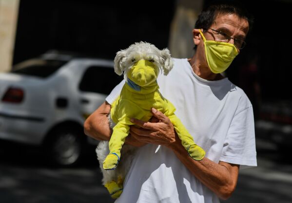 A man wears a face mask while he carries his dog with a protective suit as a preventive measure against the spread of the new coronavirus, COVID-19, in Caracas - Sputnik Азербайджан