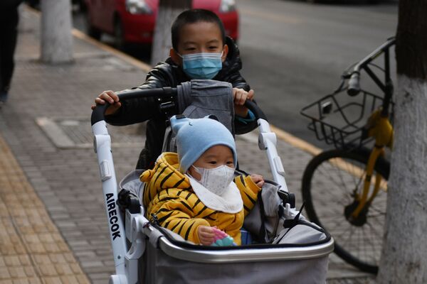 A boy wears a mask as a preventive measure against the COVID-19 coronavirus as as he pushes another child in a pram in Beijing - Sputnik Азербайджан
