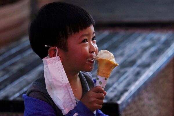 A child with a face mask eats an ice cream outside the ice cream store on its first day of opening following the coronavirus disease (COVID-19) outbreak, in Xianning, Hubei province, China - Sputnik Азербайджан