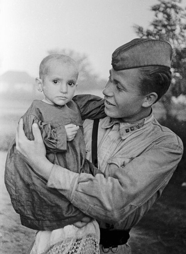 Советский офицер  держит на руках спасенную им девочку из деревни Эльхотово, 1942 год - Sputnik Азербайджан