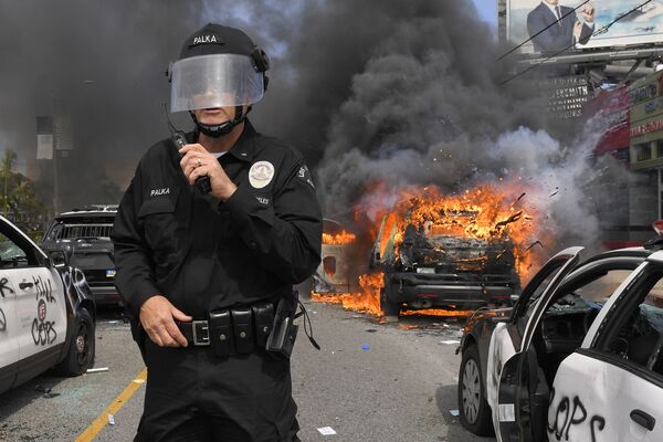 Полицейский Лос-Анджелеса на фоне горящей машины во время протестов  - Sputnik Азербайджан