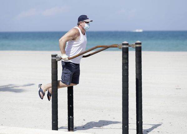 Мужчина в защитной маске во время выполнения упражнений на турнике на пляже в Голливуде, США - Sputnik Azərbaycan