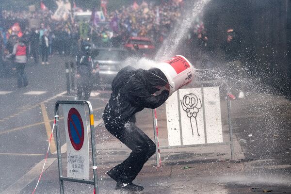 Протестующий прикрывается ведром от удара водяной пушкой, которую полицейские используют для разгона акции протеста медработников в Нанте, Франция - Sputnik Azərbaycan