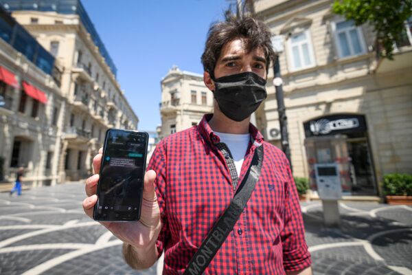 Молодой человек показывает смс-разрешение для выхода на улицу - Sputnik Азербайджан