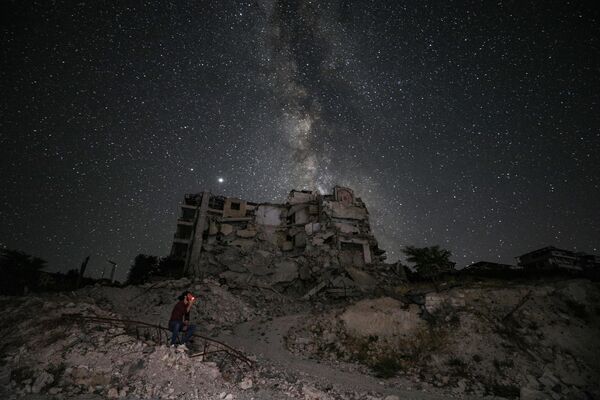 Разрушенные в результате бомбардировки здания на фоне звездного неба в сирийской провинции Идлиб - Sputnik Азербайджан